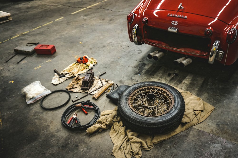Red classic car in a garage with a wheel and tools laid out